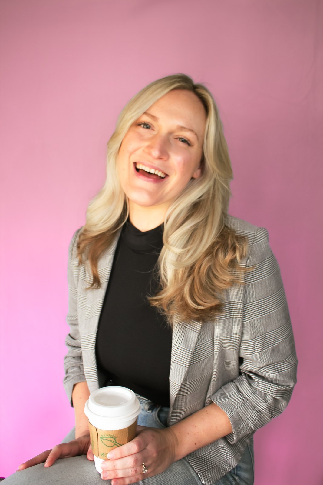 Nicollete Hillegas laughing, holding a coffee cup, against a rose backdrop
